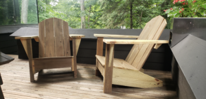 Another angle of two Adirondack chairs sitting on a wood Veranda. Side profile. Humming Bird Exclusives.